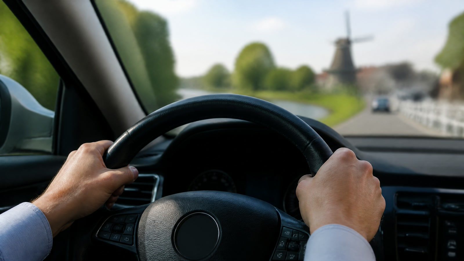 Persoon houdt het stuur vast tijdens het autorijden met uitzicht op een weg en een molen